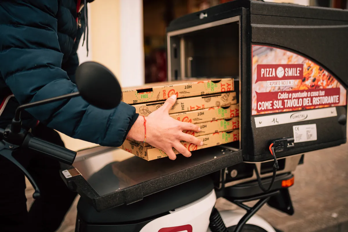 Il rider carica i cartoni delle pizze nel bauletto termico Pizza Smile dello scooter