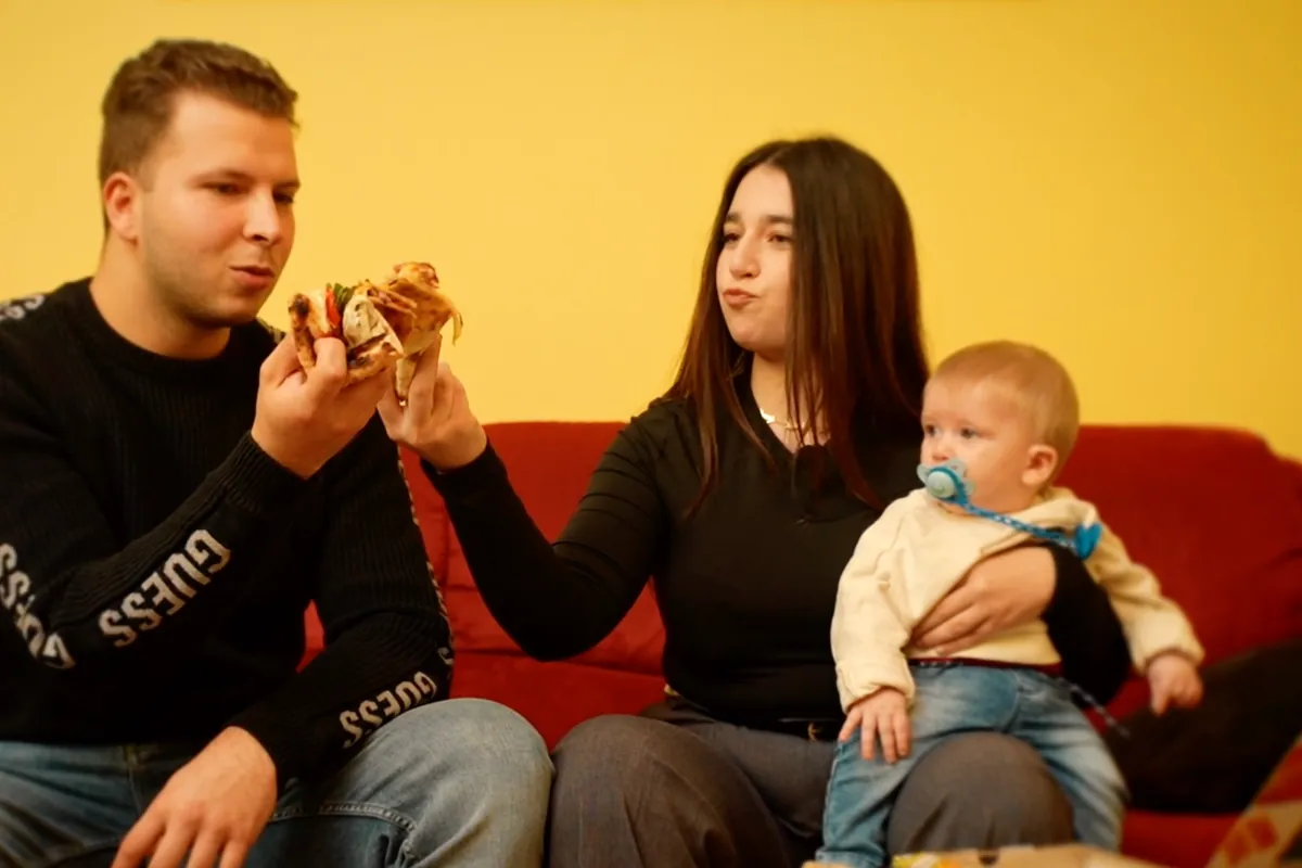 Una giovane famiglia sul divano rosso mangia la pizza Pizza Smile, con il bambino in braccio alla mamma