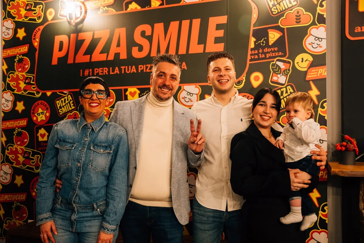 Persone sorridenti con un bambino in braccio davanti alla parete Pizza Smile, dentro una delle nostre pizzerie