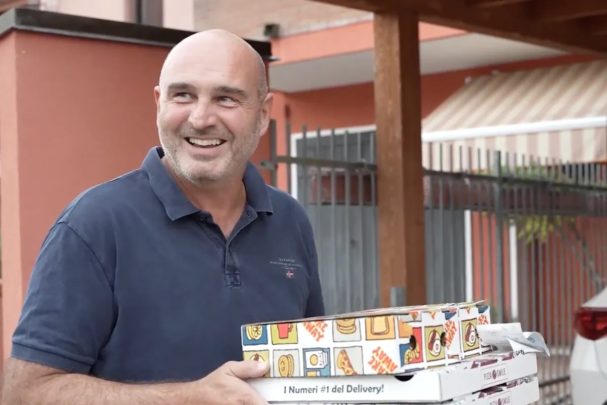 Un cliente sorridente davanti a casa con in mano i cartoni delle pizze Pizza Smile appena consegnati