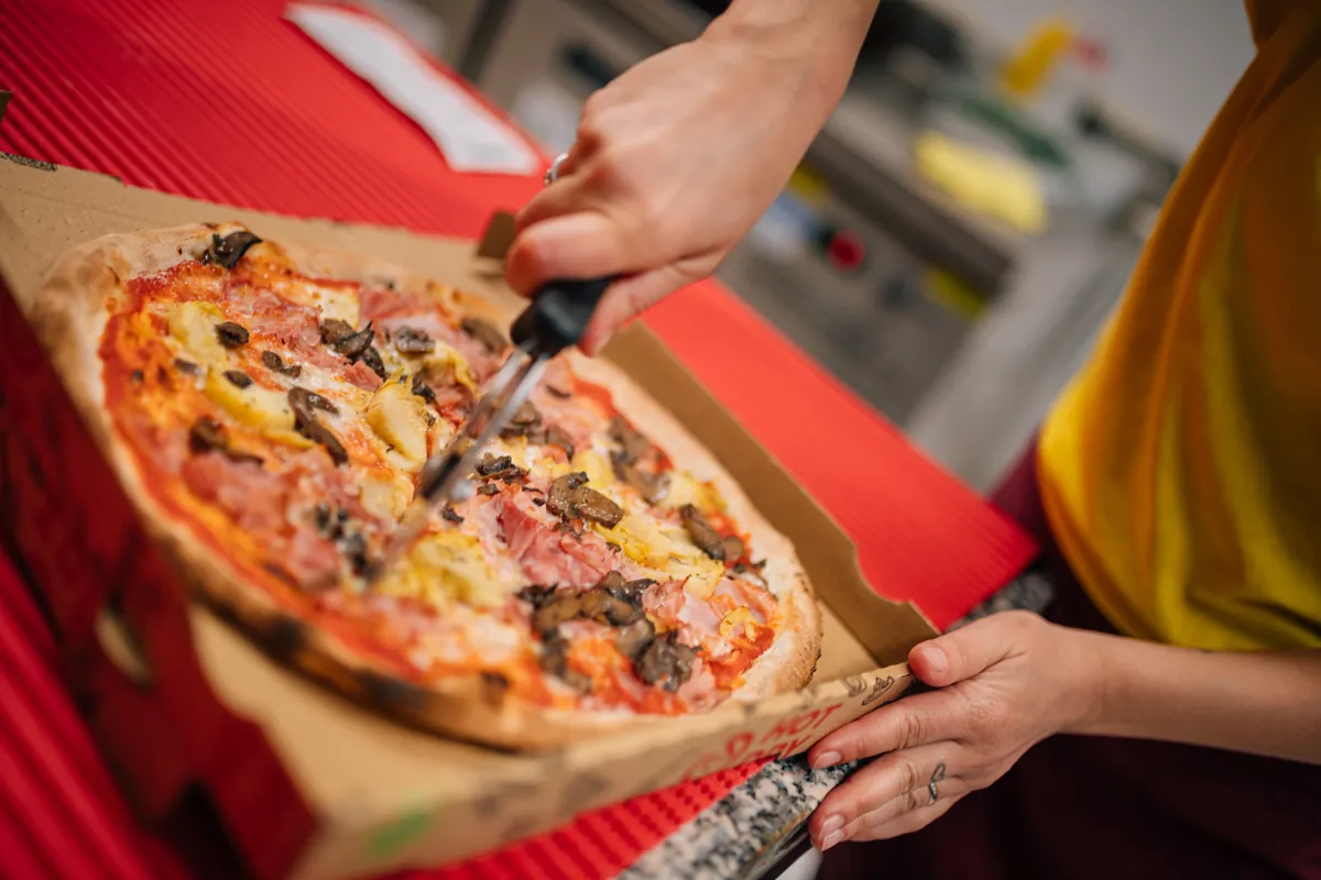Una pizza con funghi e prosciutto viene tagliata nel cartone con la rotella