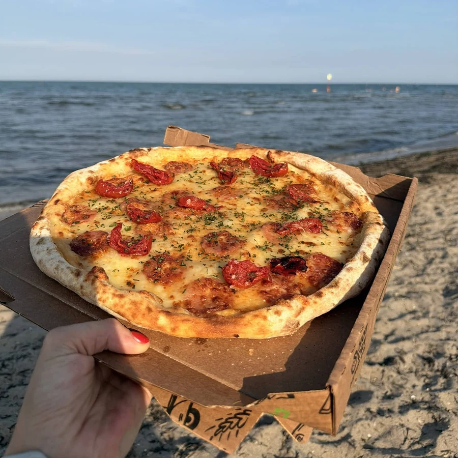 Pizza Smile's Sunkissed pizza, with confit cherry tomatoes and spicy salami, photographed on the beach.